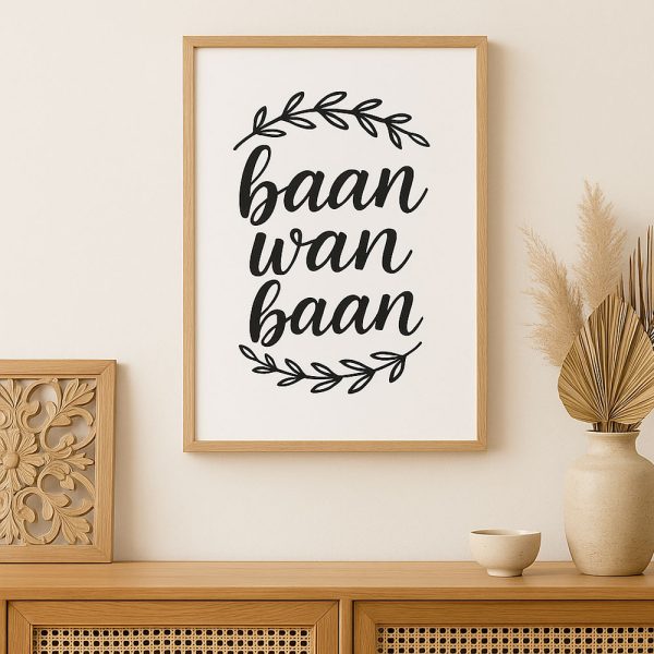 A black and white minimalist poster with the text "Baan Wan Baan" with laurel leafs above and below. Hanging in a wooden frame on a wall in a modern home with Thai inspired decor.